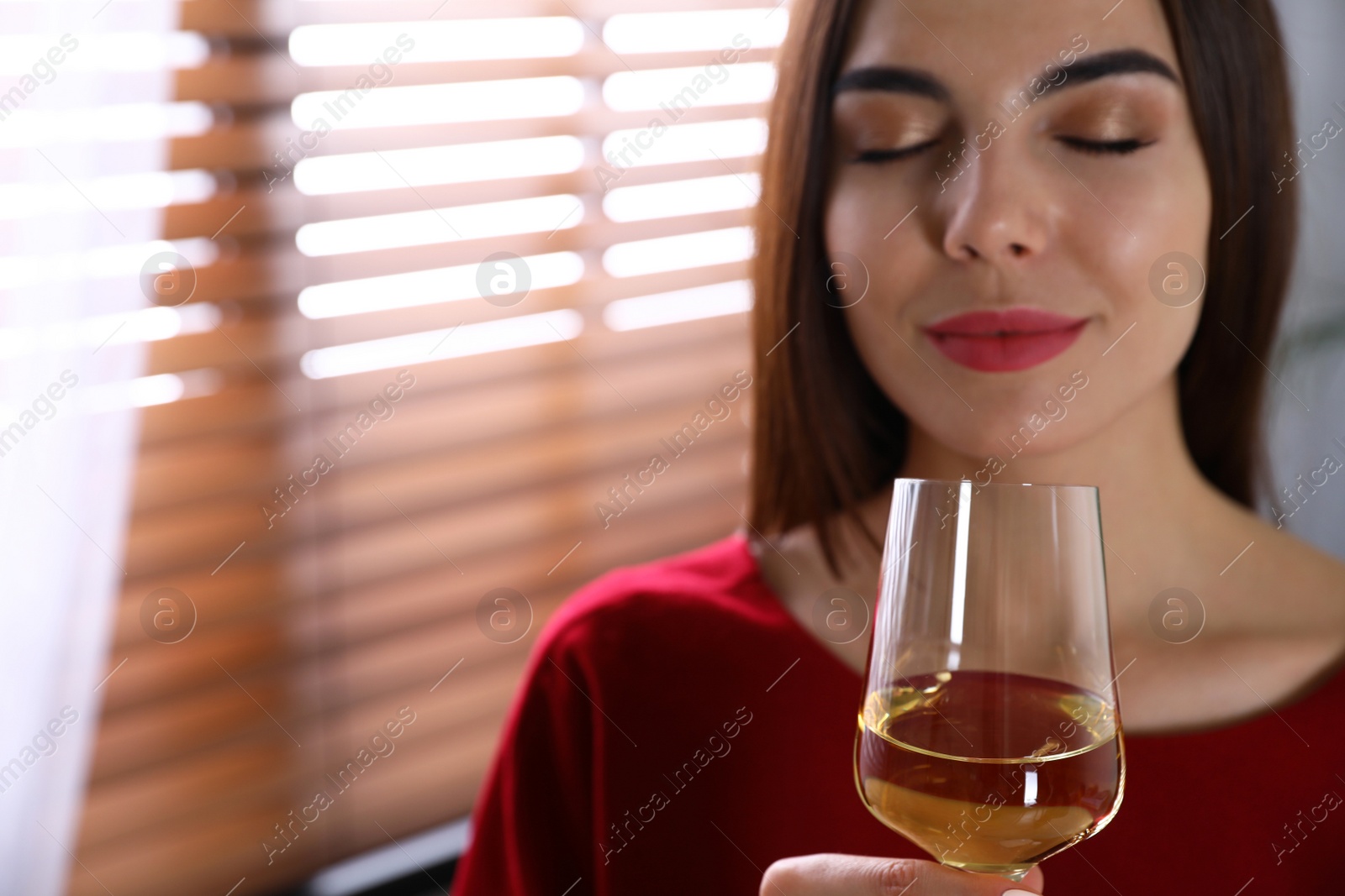 Photo of Beautiful young woman with glass of luxury white wine indoors, closeup view. Space for text