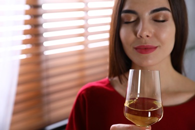 Beautiful young woman with glass of luxury white wine indoors, closeup view. Space for text