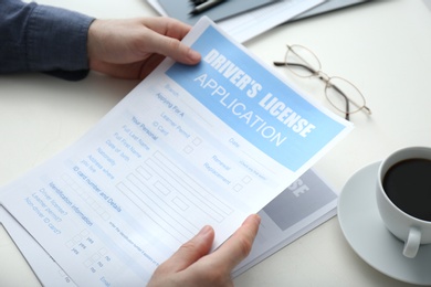 Photo of Man with driver's license application form and cup of coffee at white table, closeup