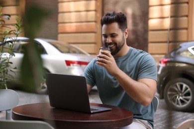 Photo of Handsome man with laptop drinking coffee at table in outdoor cafe