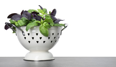 Photo of Colander with fresh basil leaves on grey table against white background. Space for text