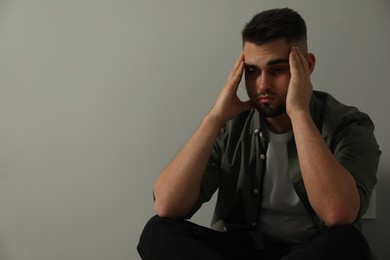 Sad man sitting near light grey wall. Space for text