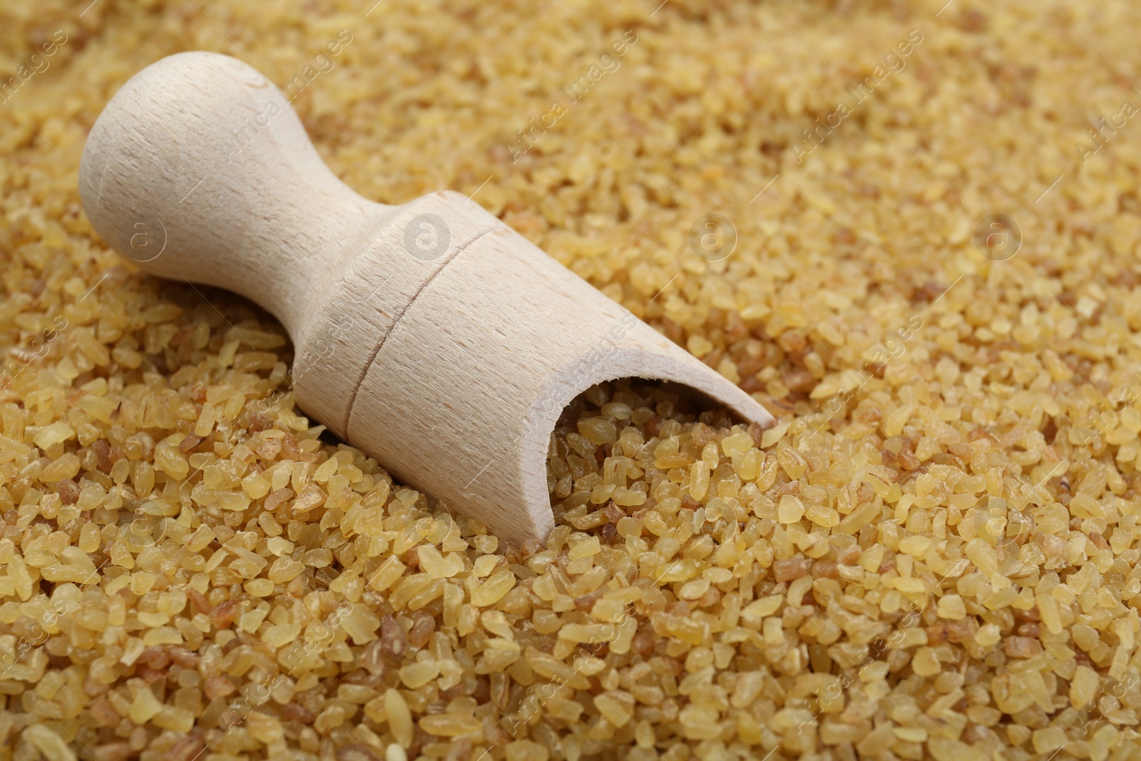 Photo of Wooden scoop on pile of uncooked bulgur, closeup view