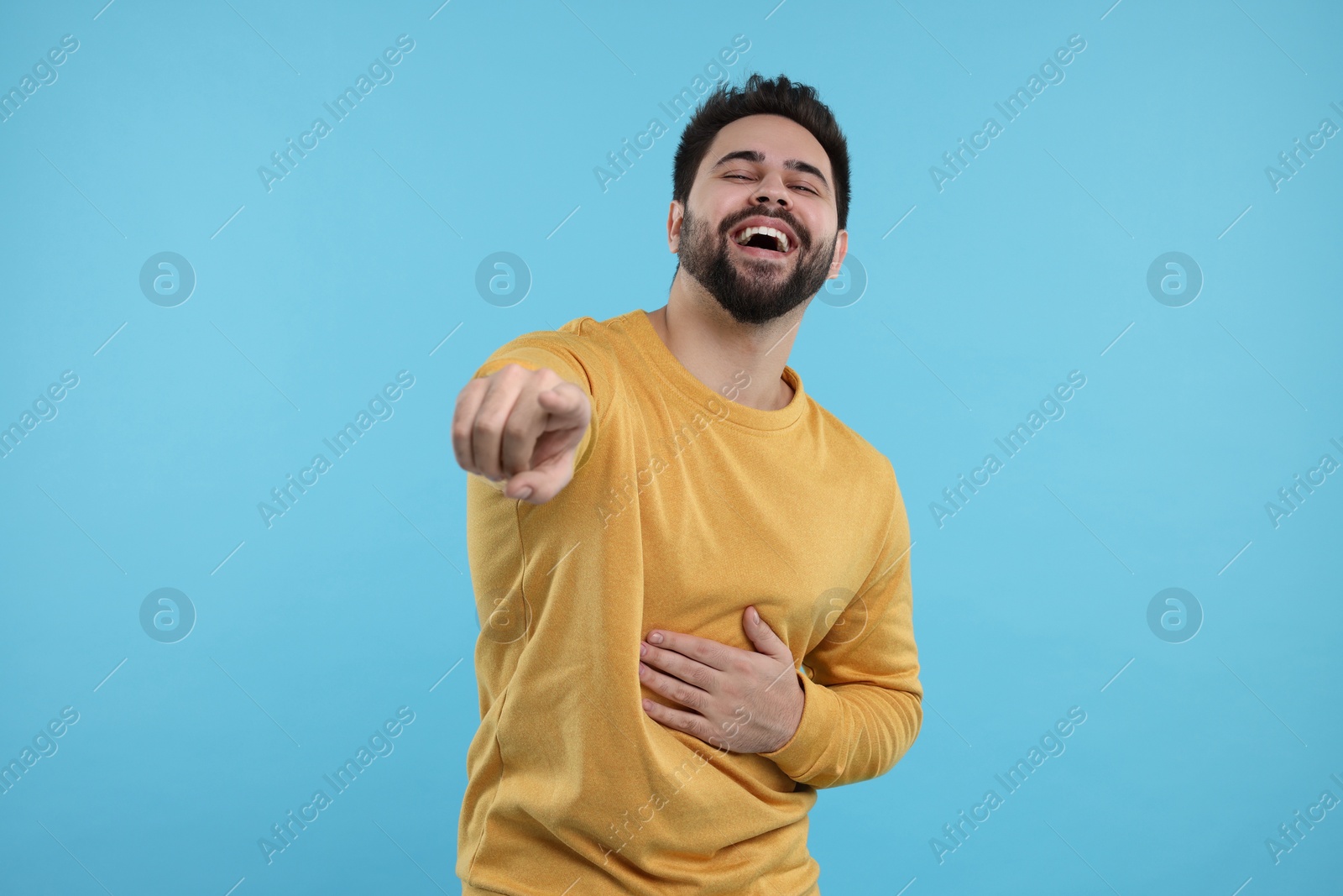 Photo of Handsome young man laughing while pointing at something on light blue background