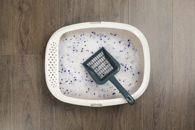 Photo of Cat litter tray with filler and scoop on wooden floor, top view