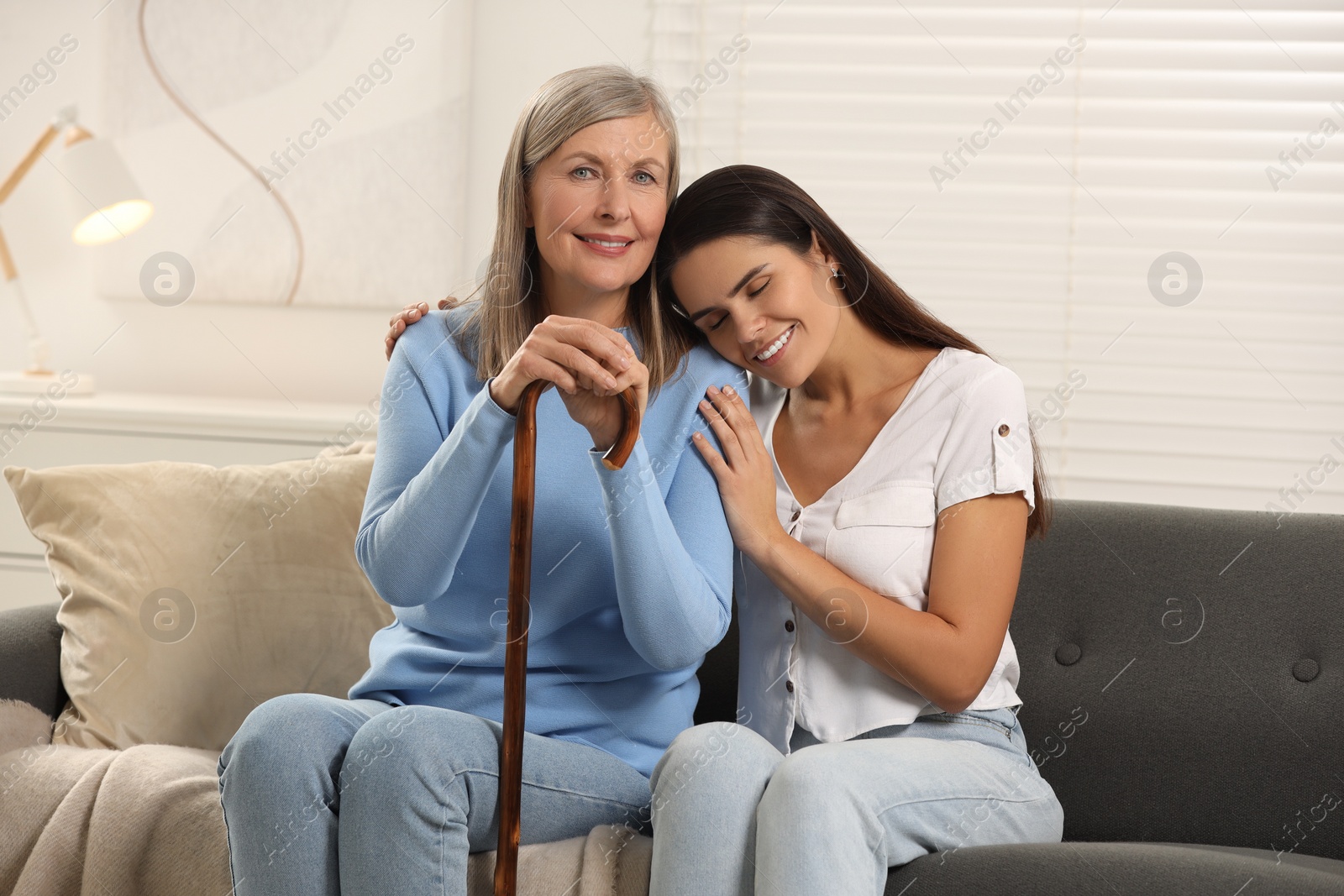 Photo of Mature lady with walking cane and young woman on sofa at home