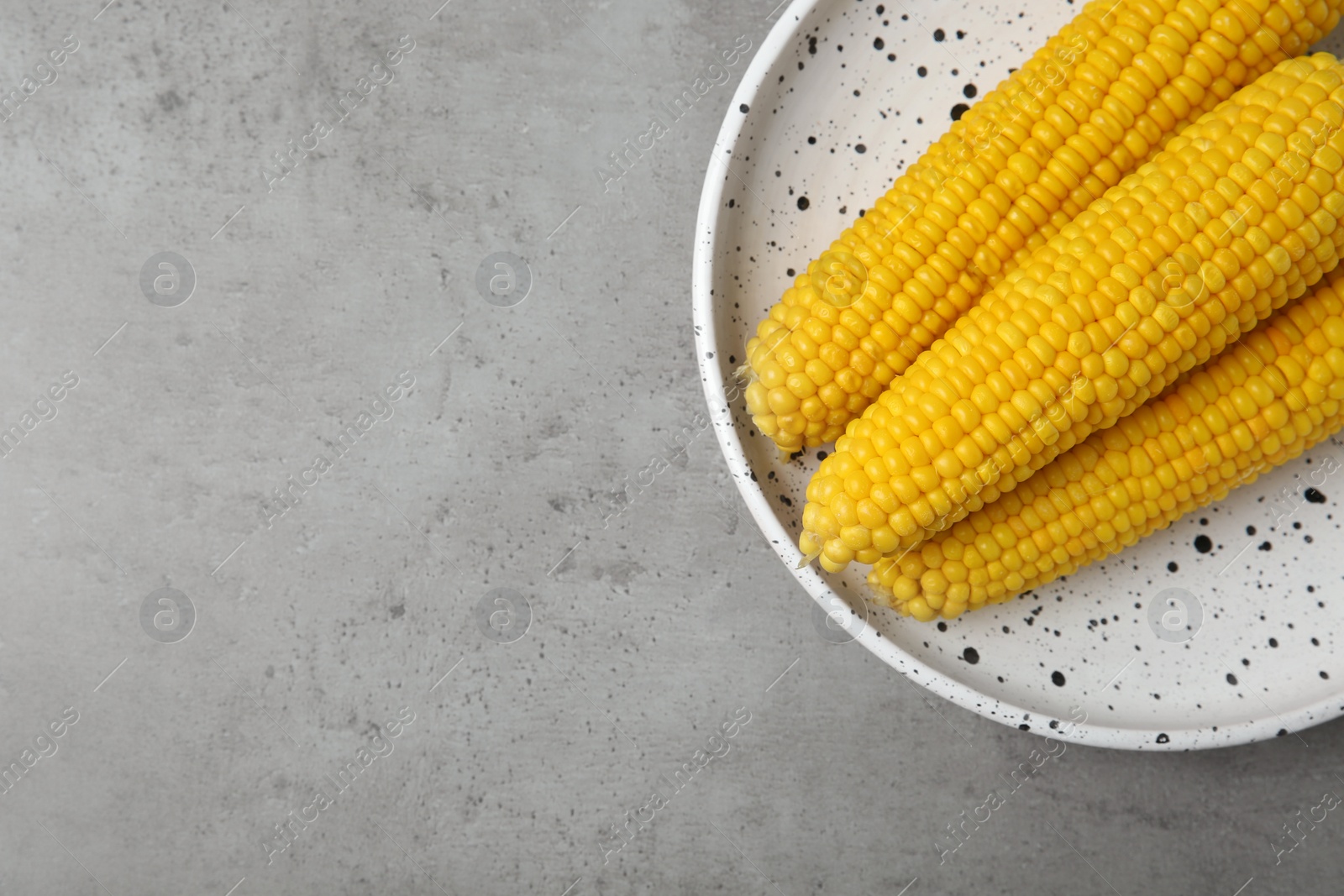 Photo of Plate with tasty boiled corn cobs on light grey table, top view. Space for text