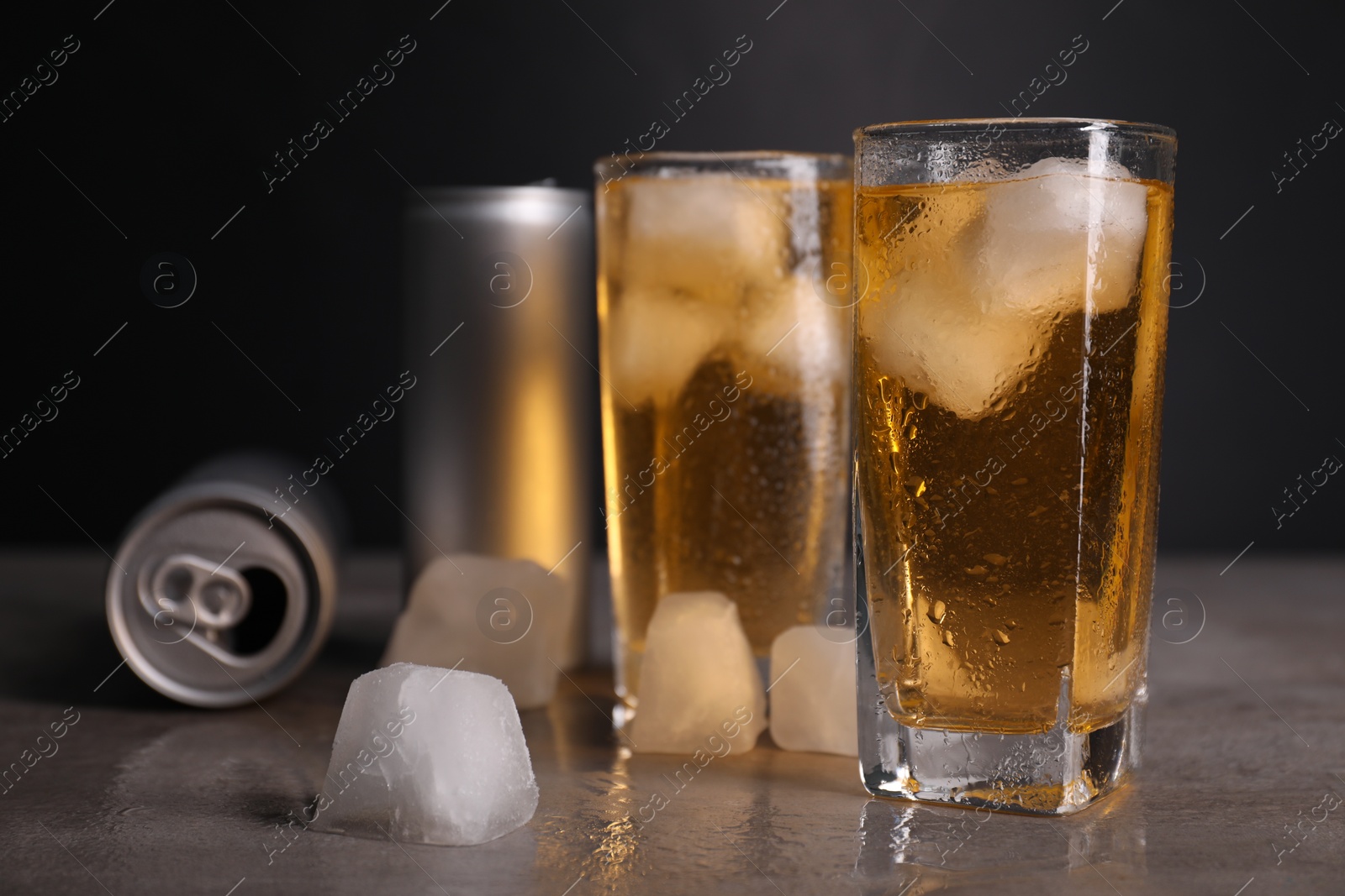 Photo of Tasty energy drink with ice cubes in glasses and aluminium cans on grey table, closeup