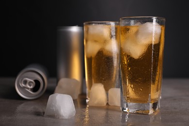 Photo of Tasty energy drink with ice cubes in glasses and aluminium cans on grey table, closeup