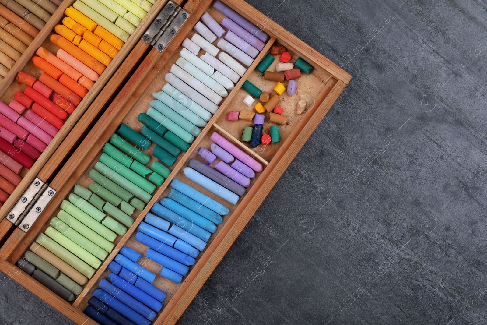 Photo of Set of colorful pastels in wooden box on grey stone table, top view with space for text. Drawing materials