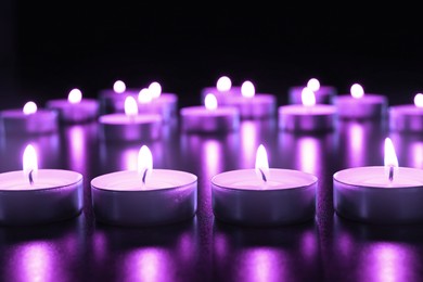 Beautiful burning violet candles on black background. Funeral attributes