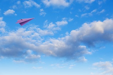 Image of Purple paper plane flying in blue sky with clouds