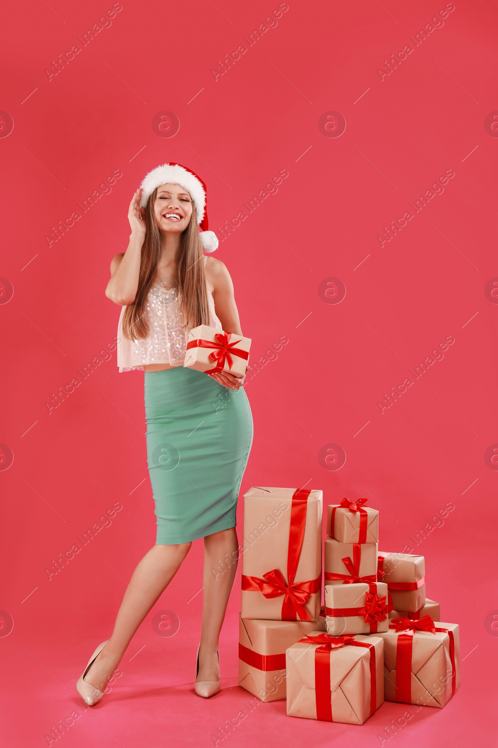 Photo of Happy young woman in Santa hat with Christmas gifts on pink background