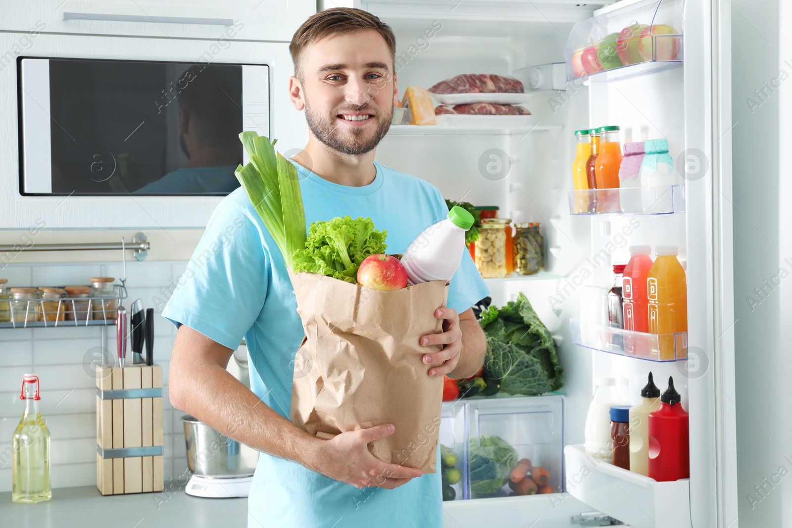 Photo of Man with bag of products standing near refrigerator in kitchen