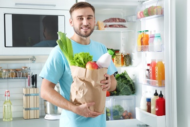 Photo of Man with bag of products standing near refrigerator in kitchen