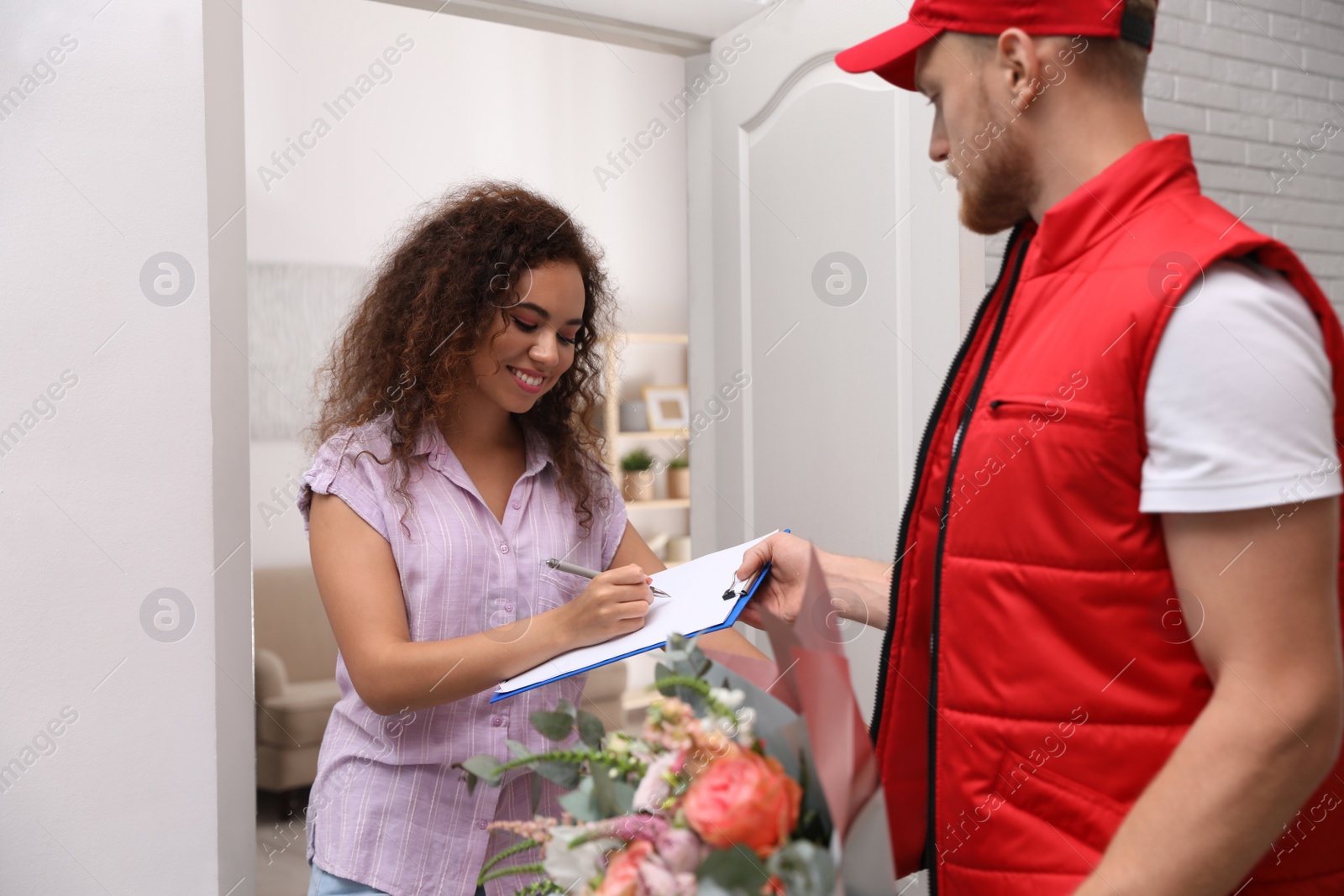 Photo of African-American woman receiving flower bouquet from delivery man indoors