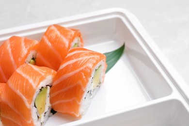 Photo of Delicious sushi rolls with salmon in plastic container, closeup. Food delivery