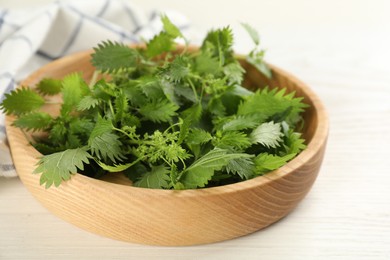 Photo of Wooden plate with fresh stinging nettle leaves on white table, closeup