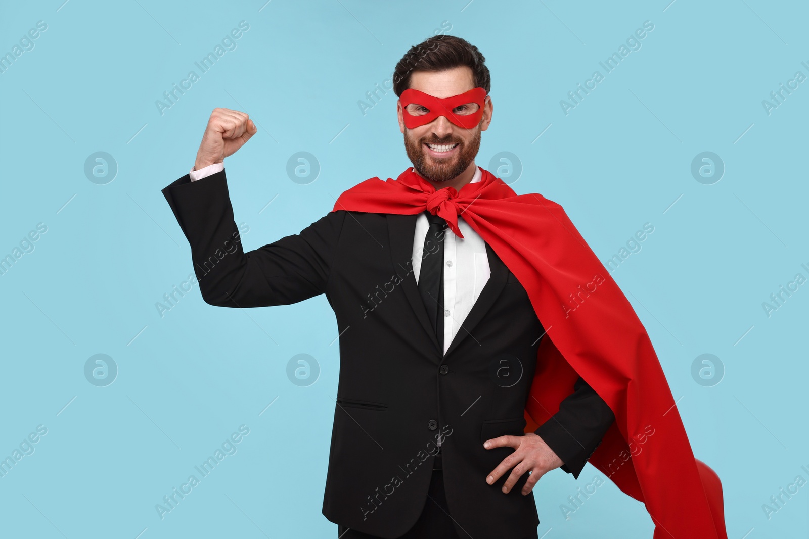 Photo of Businessman wearing red superhero cape and mask on light blue background