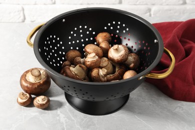 Raw mushrooms in black colander on marble table