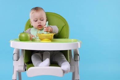 Cute little baby eating healthy food in high chair on light blue background, space for text