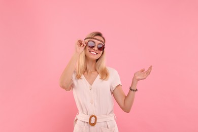 Portrait of smiling hippie woman in sunglasses on pink background