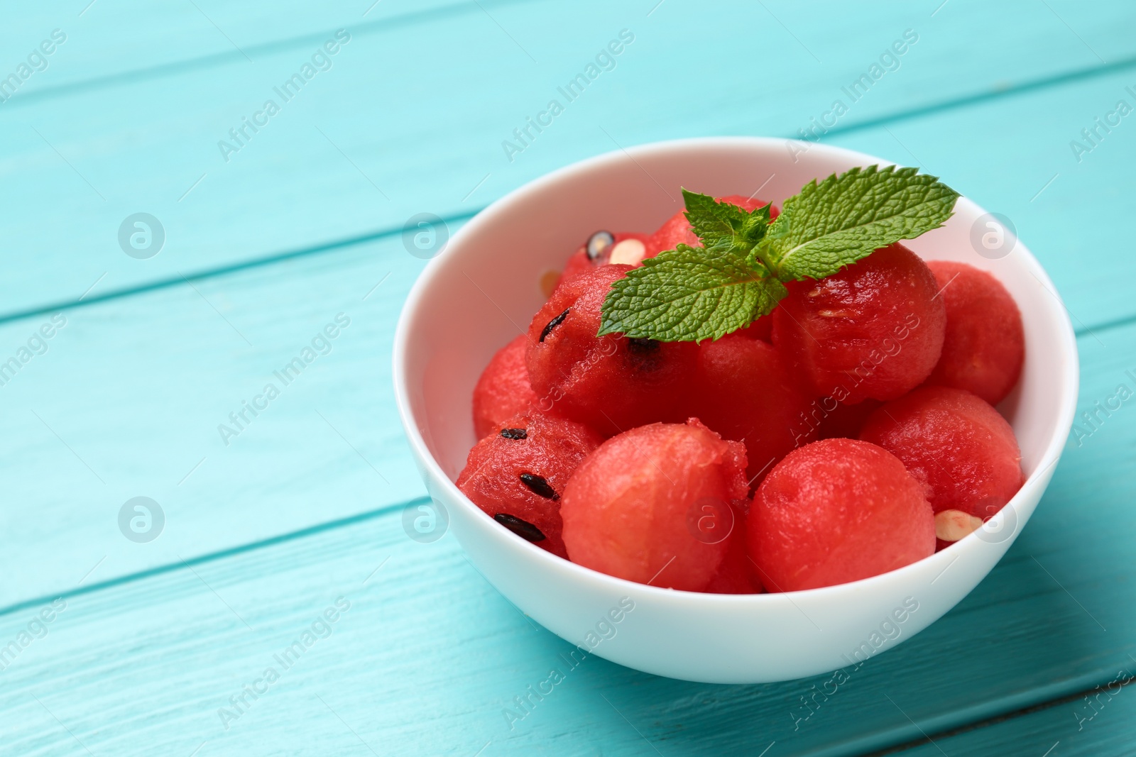 Photo of Bowl of watermelon balls with mint on light blue wooden table