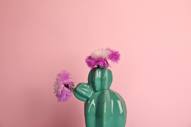 Trendy cactus shaped ceramic vase with flowers on color background