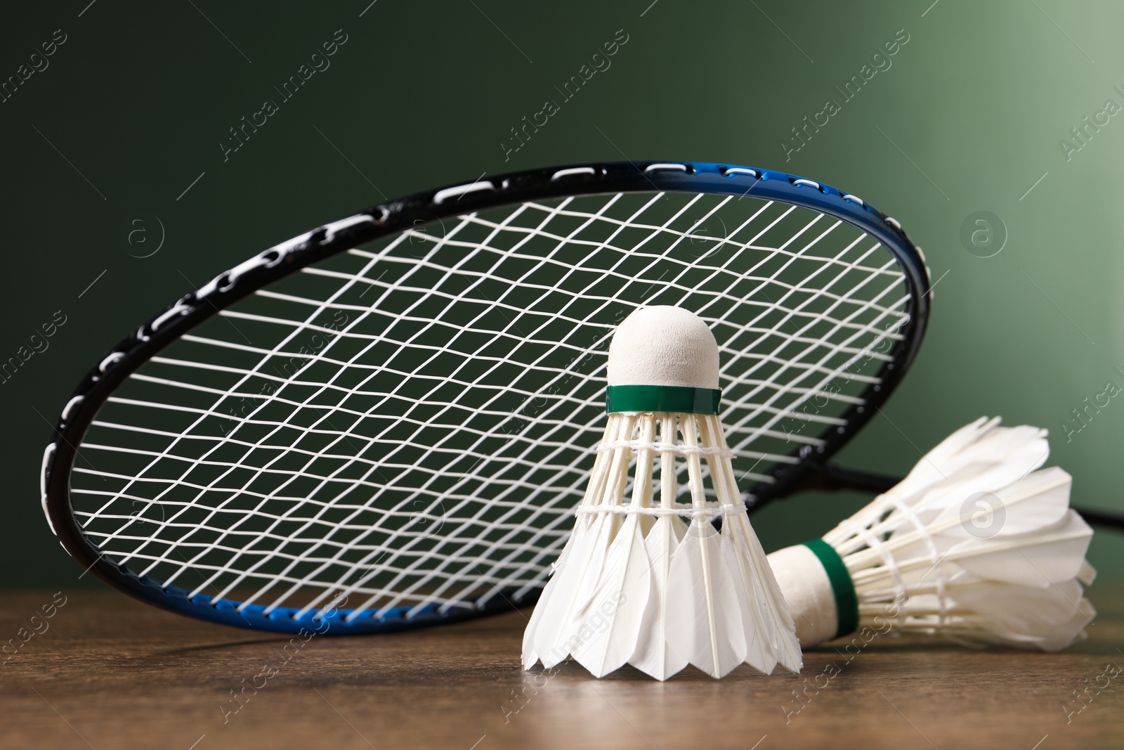 Photo of Feather badminton shuttlecocks and racket on wooden table against green background, closeup. Space for text