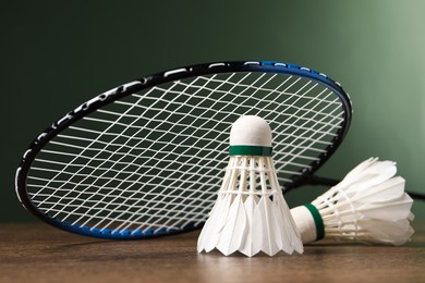 Feather badminton shuttlecocks and racket on wooden table against green background, closeup. Space for text