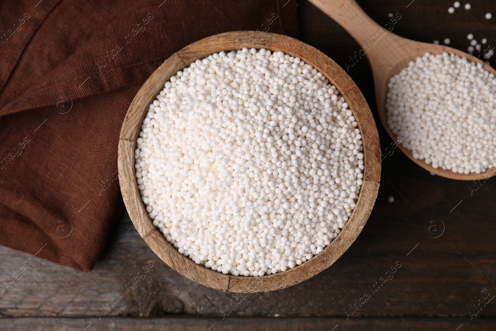 Photo of Tapioca pearls in bowl and spoon on wooden table, flat lay