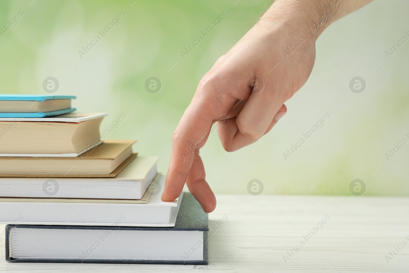 Photo of Man climbing up stairs of books with fingers on white wooden table against blurred background, closeup