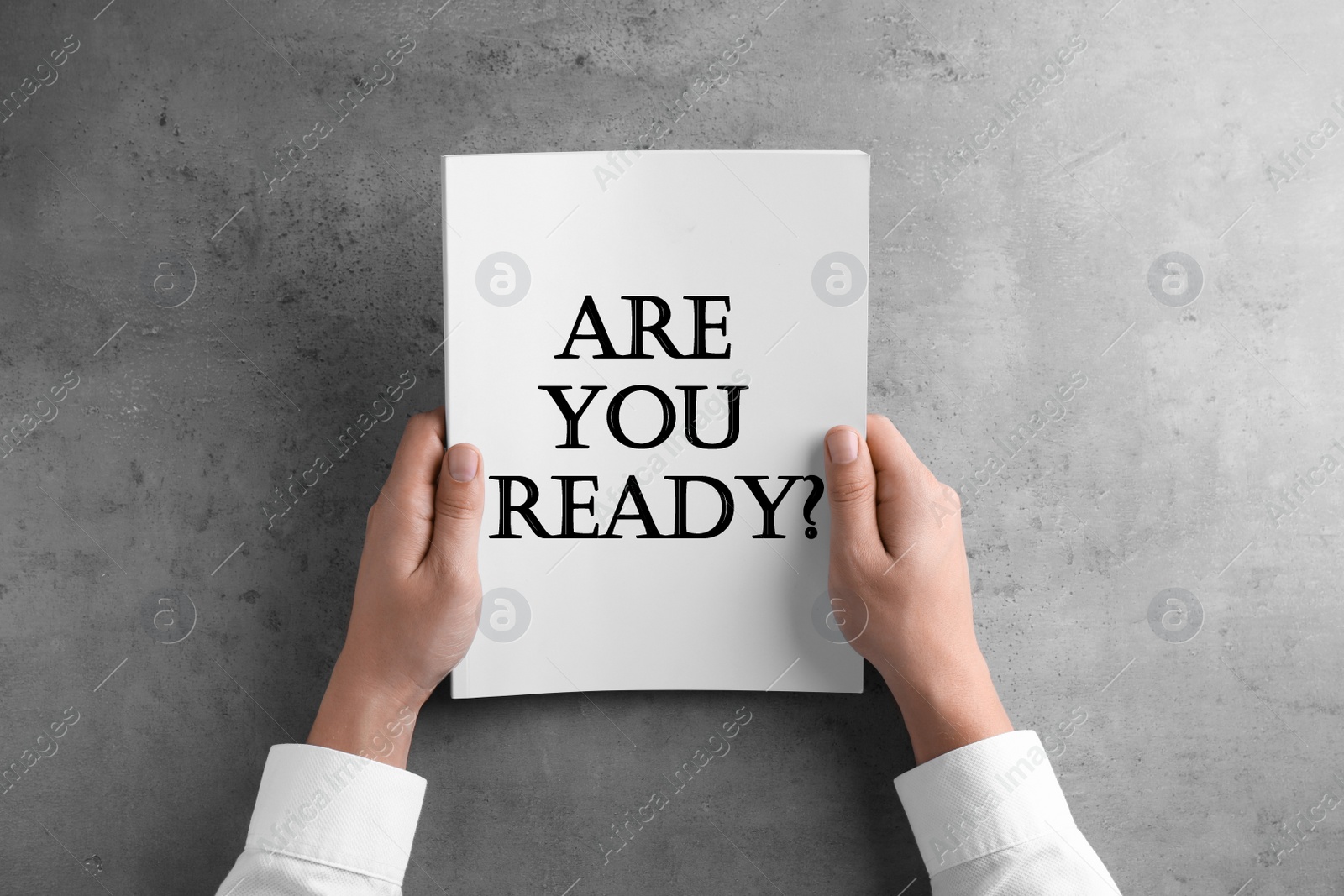 Image of Man holding paper sheet with text Are You Ready? at grey table, top view