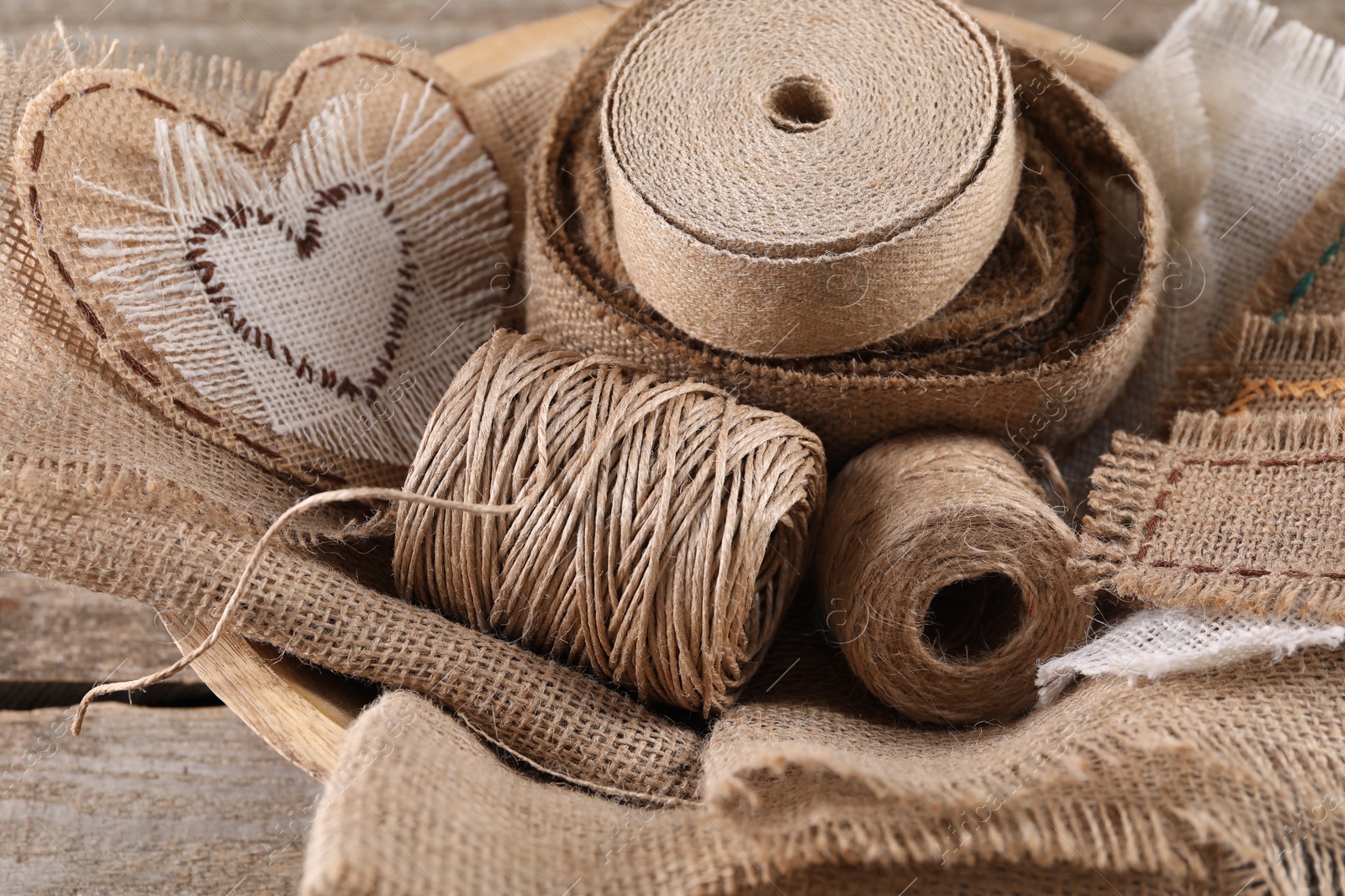 Photo of Pieces of burlap fabric and spools of twine on wooden table, closeup