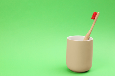 Bamboo toothbrush in holder on green background, space for text