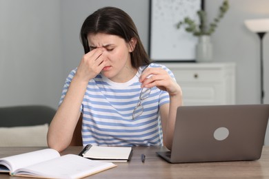 Overwhelmed woman sitting with laptop at table indoors