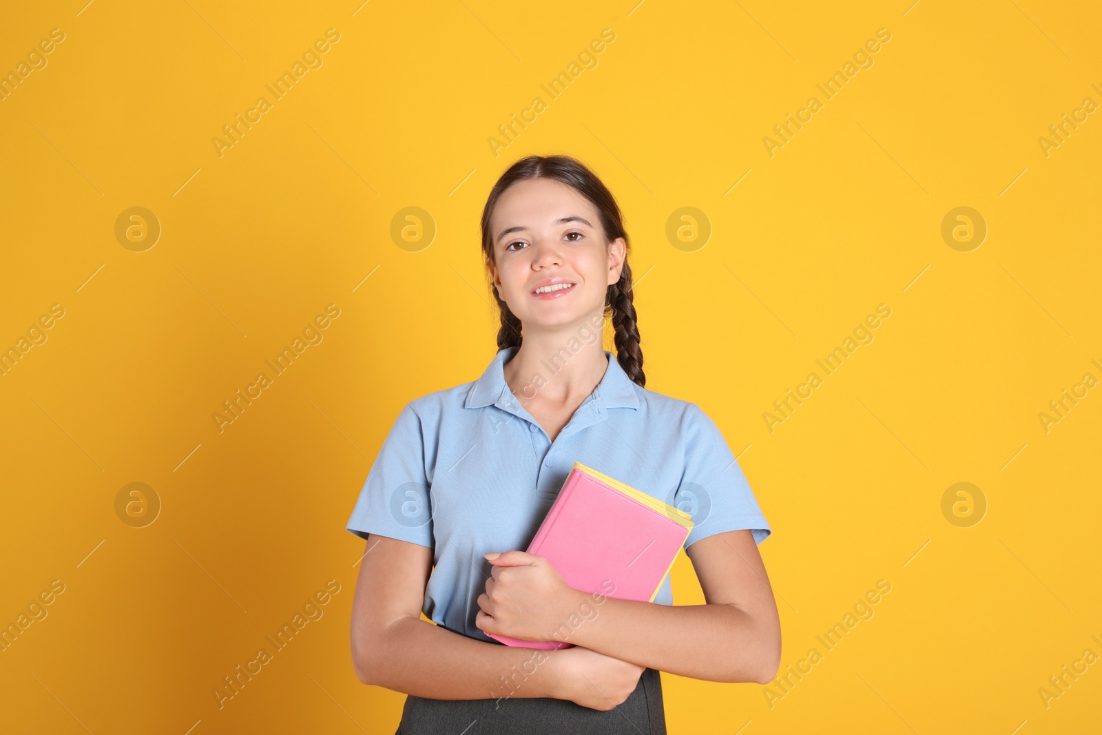 Photo of Teenage girl in school uniform with books on orange background