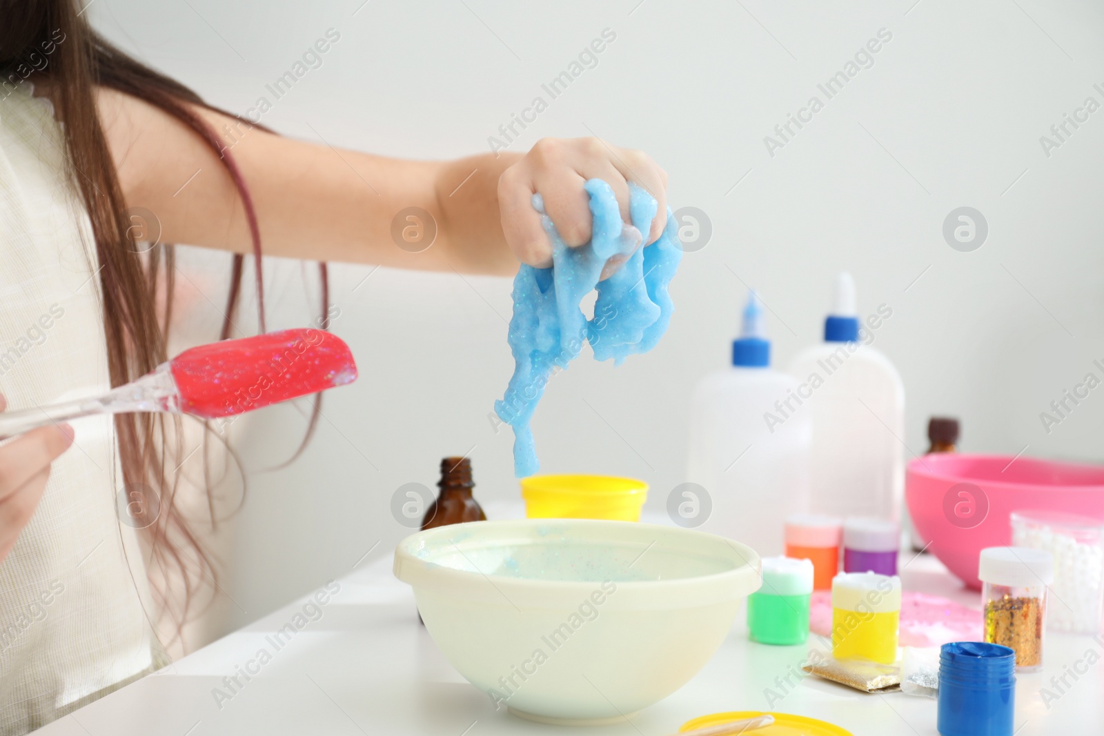 Photo of Little girl making DIY slime toy at table in room, closeup