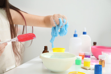 Little girl making DIY slime toy at table in room, closeup