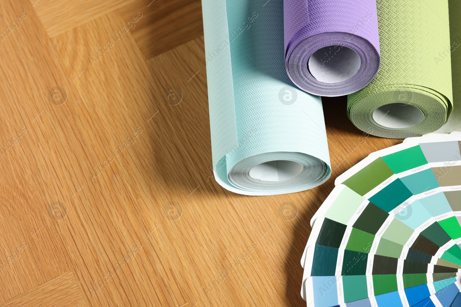 Photo of Different wallpaper rolls and color palette samples on wooden table, space for text