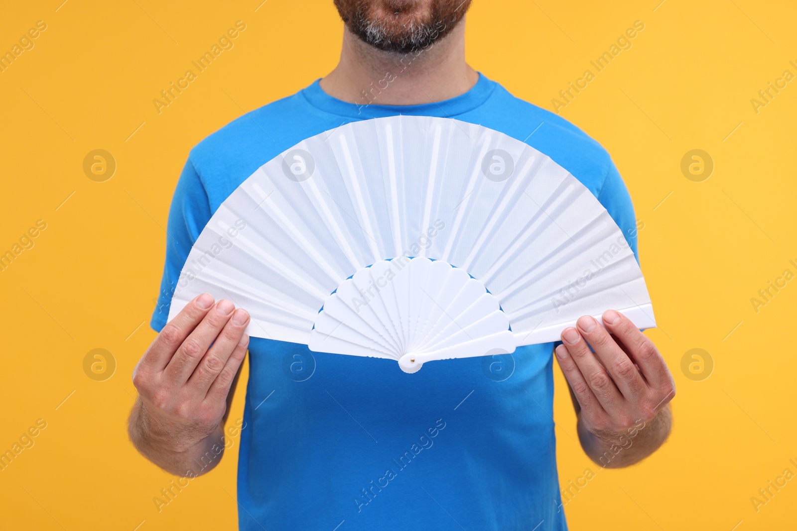 Photo of Man holding hand fan on orange background, closeup