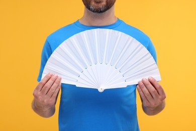 Photo of Man holding hand fan on orange background, closeup
