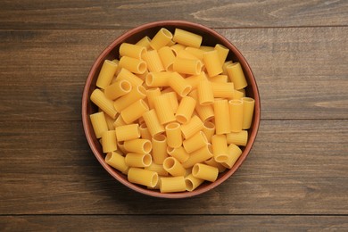 Photo of Raw rigatoni pasta in bowl on wooden table, top view