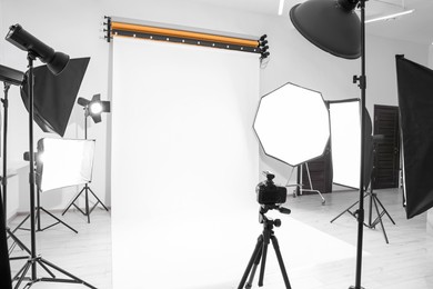 Photo of Tripod with camera and professional lighting equipment in modern photo studio