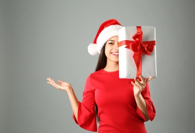 Photo of Young beautiful woman in Santa hat with gift box on grey background. Christmas celebration