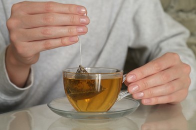 Photo of Woman taking tea bag out of cup at table indoors, closeup
