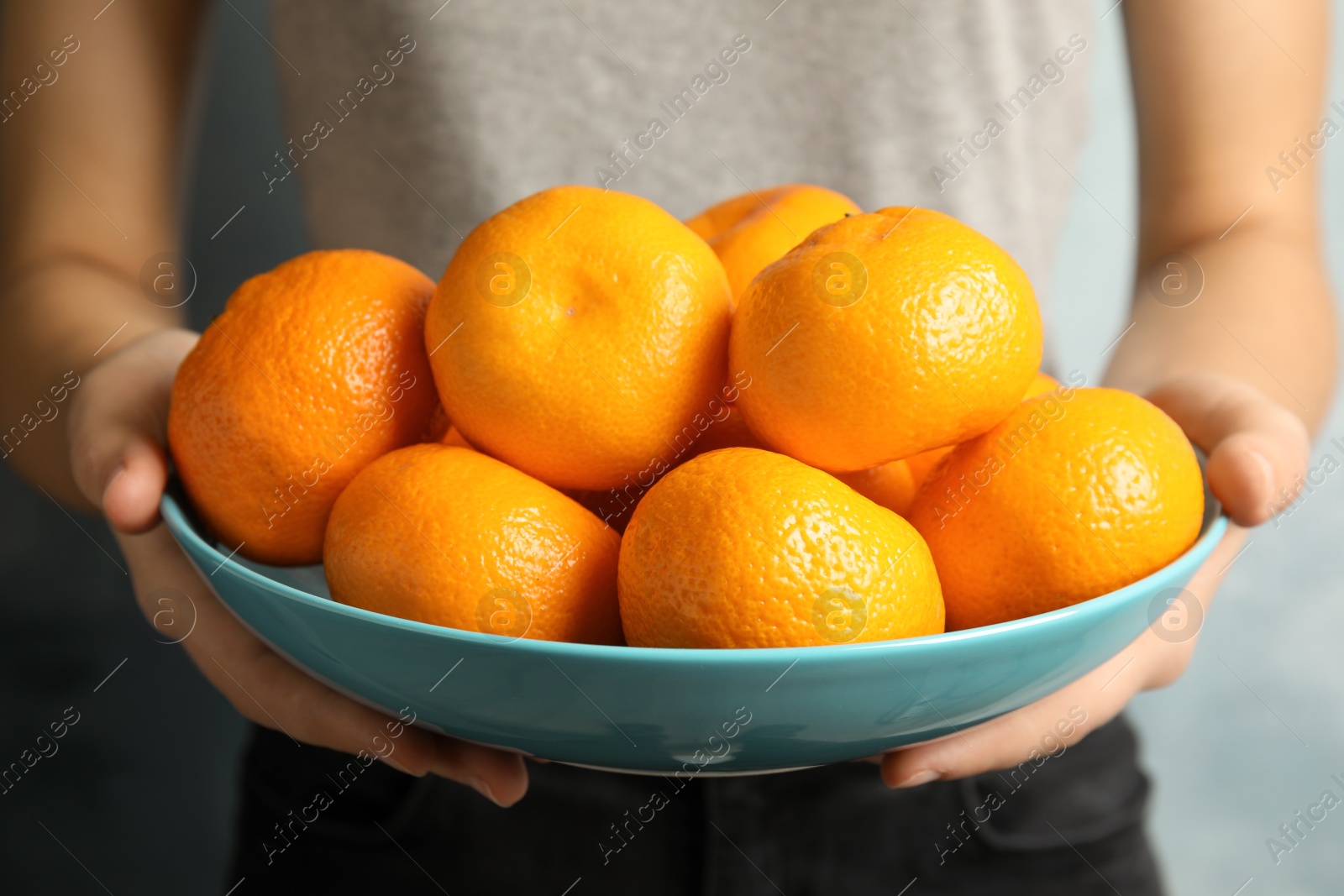 Photo of Woman holding bowl of ripe tangerines, closeup