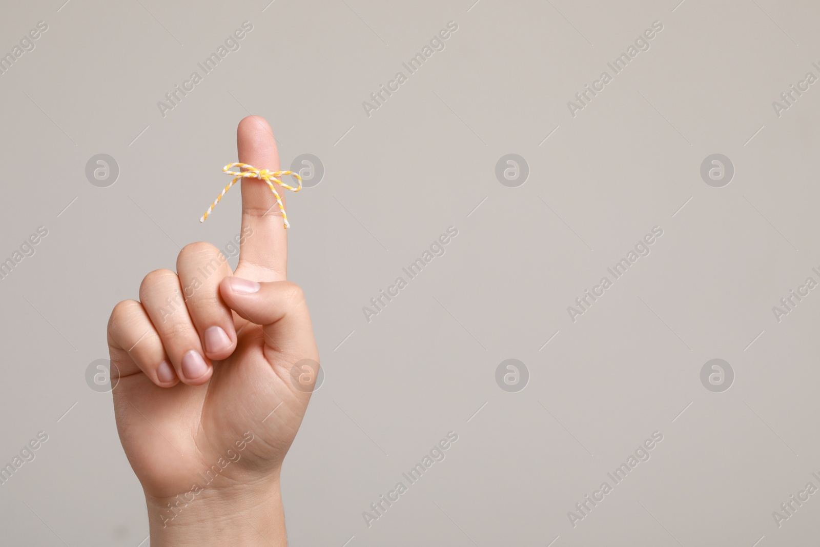 Photo of Man showing index finger with tied bow as reminder on light grey background, closeup. Space for text