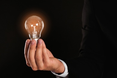 Photo of Businessman holding lamp bulb against dark background
