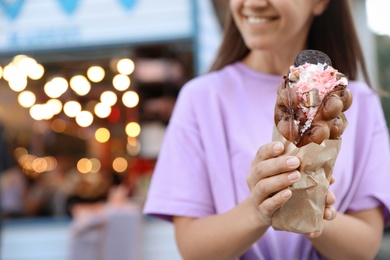 Photo of Young woman holding delicious sweet bubble waffle with ice cream outdoors, closeup